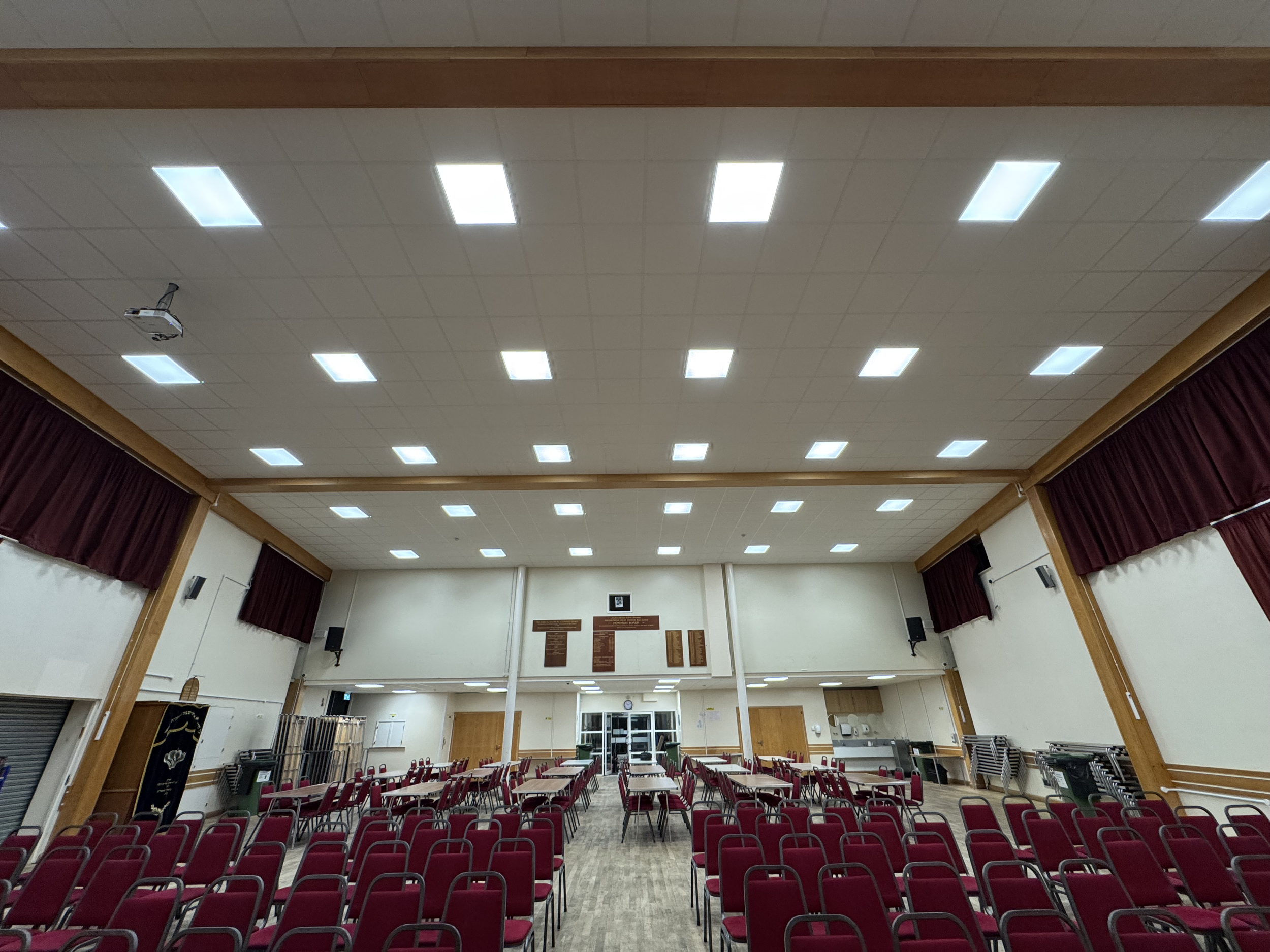 Large indoor hall with rows of red chairs, a stage at the front, and ceiling lights.