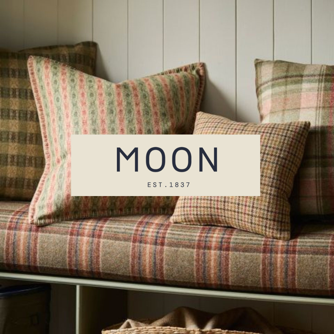 A cozy room with a plaid sofa and multiple patterned throw pillows in warm tones, with a white paneled wall in the background and a box underneath the sofa.