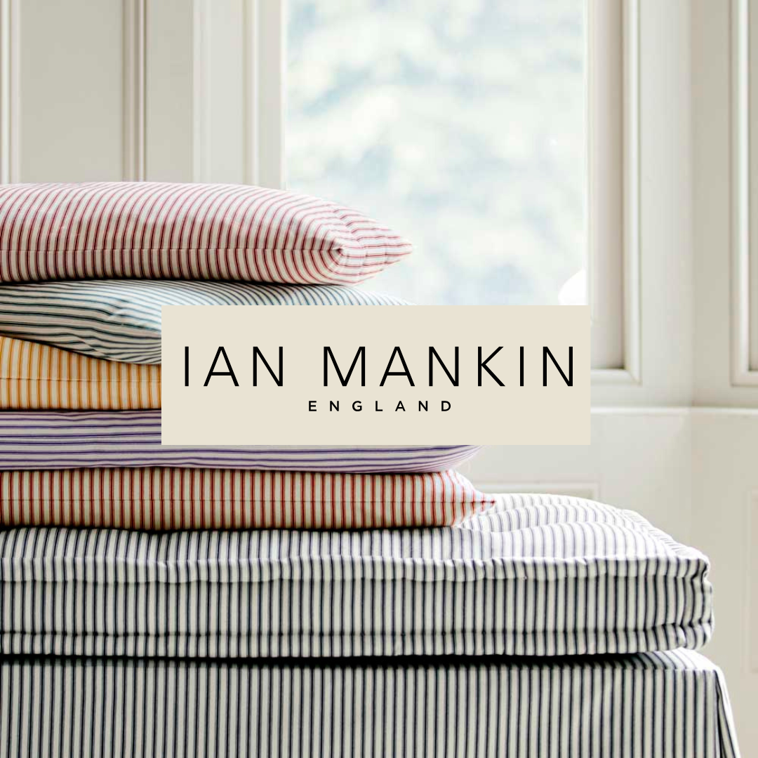 A stack of neatly folded striped bed linens on a bed near a window with white trim in natural light.
