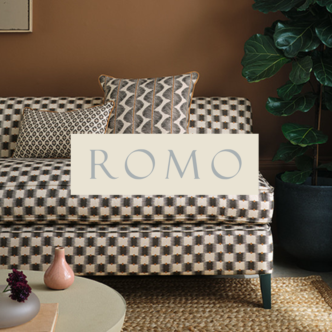 Interior living room with a patterned checkered sofa, two decorative pillows, a large green leafy plant in a black pot, and a round cream-colored coffee table with vases, set against a brown wall.