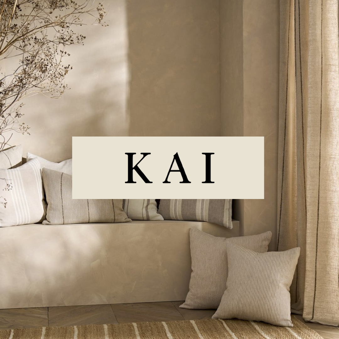 A neutral-colored living room corner with a built-in bench, striped and solid pillows, curtains, and a dried tree branch decor, with the Greek letters KAI in the center.
