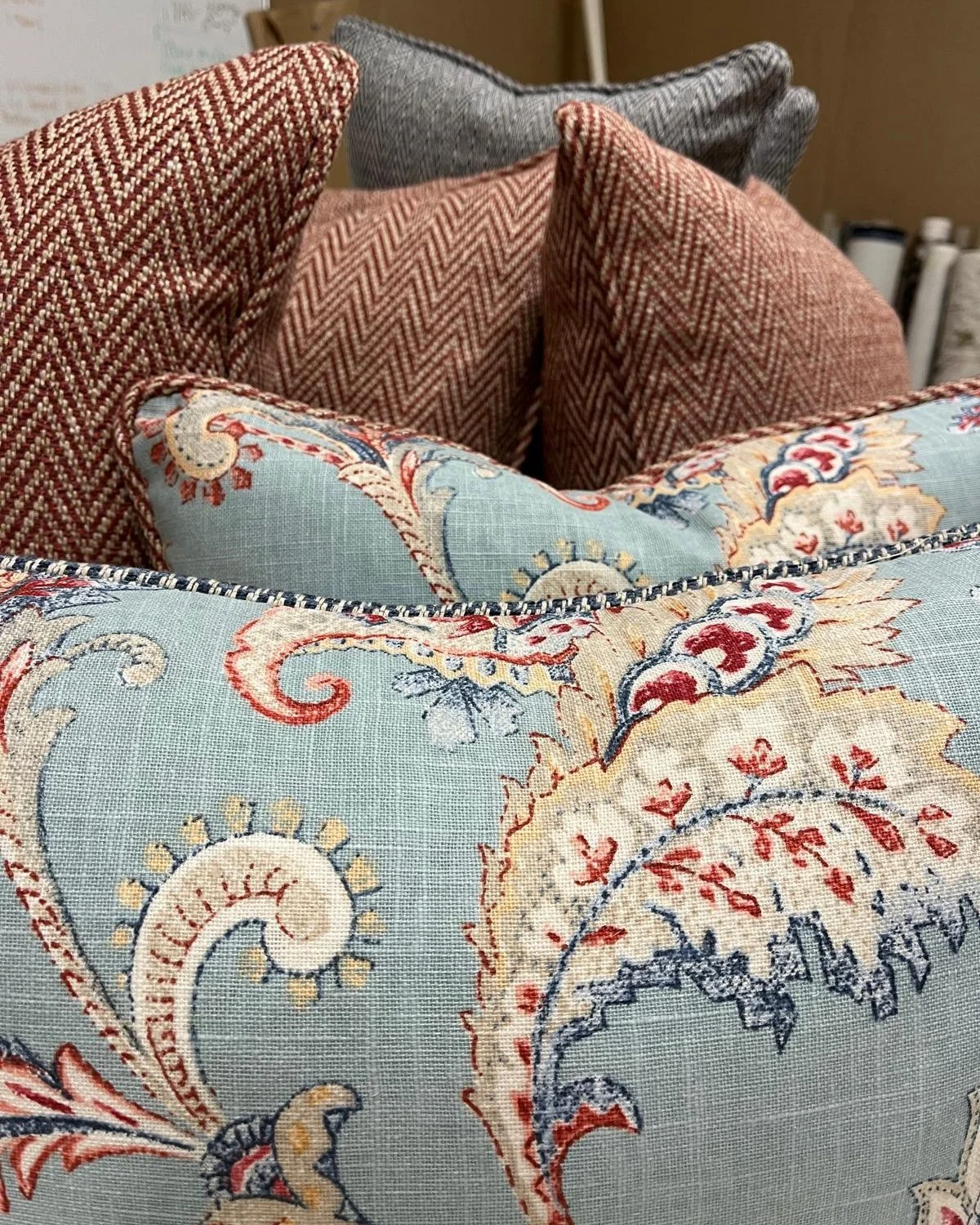 Close-up of decorative pillows with various patterns including paisley, herringbone, and chevron on a couch.