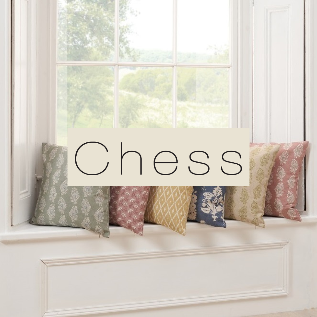 A window seat with six decorative pillows featuring various pastel and floral patterns, and the word 'Chess' overlayed in the center.