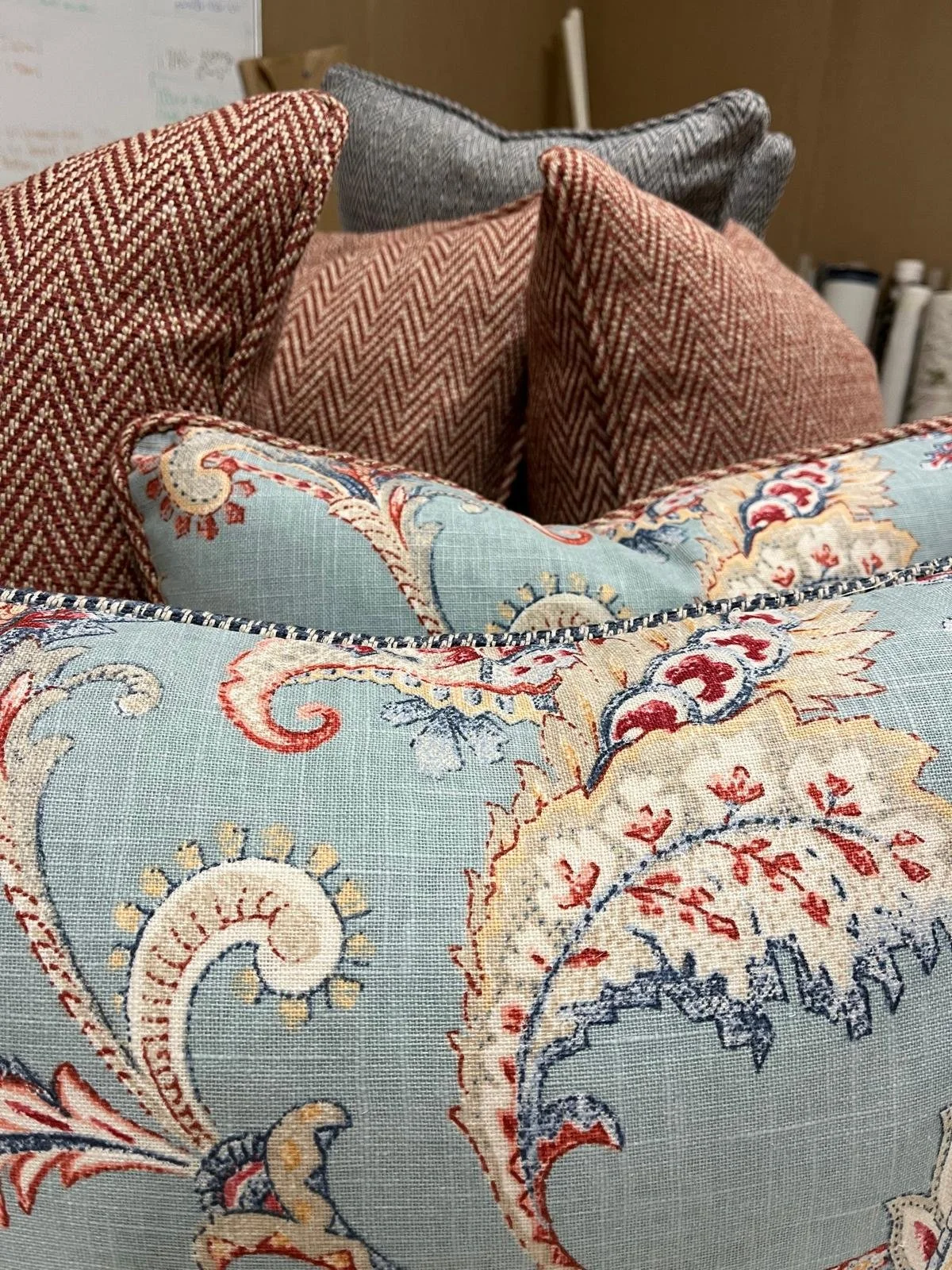 Close-up of decorative throw pillows with various patterns and colors, including floral and geometric prints, arranged on a surface in an indoor setting.