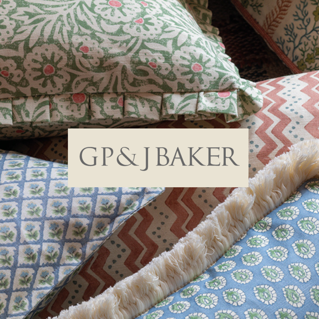 Close-up of decorative pillows with floral and geometric patterns and a label reading 'GP&J BAKER' on top.