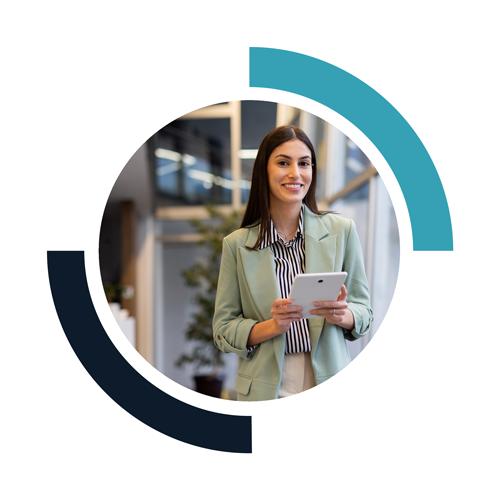 A young woman in business attire holding a tablet device, standing in a modern office environment.