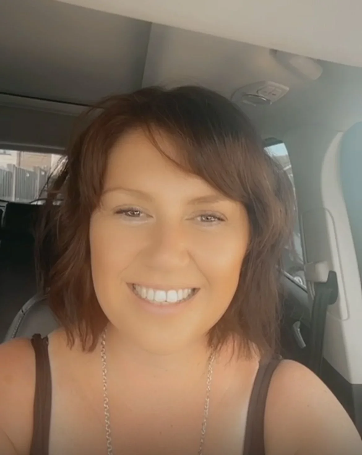 A woman with short brown hair smiling for a selfie inside a vehicle.
