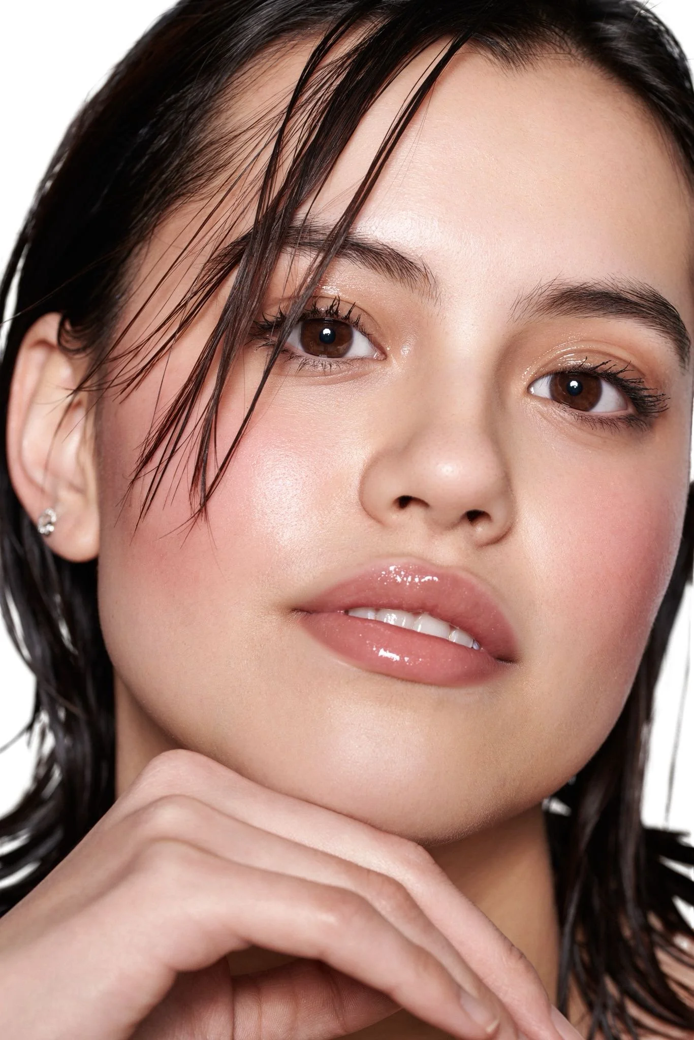 Close-up of a woman's face with wet hair, natural makeup, and glossy lips, resting her chin on her hand.