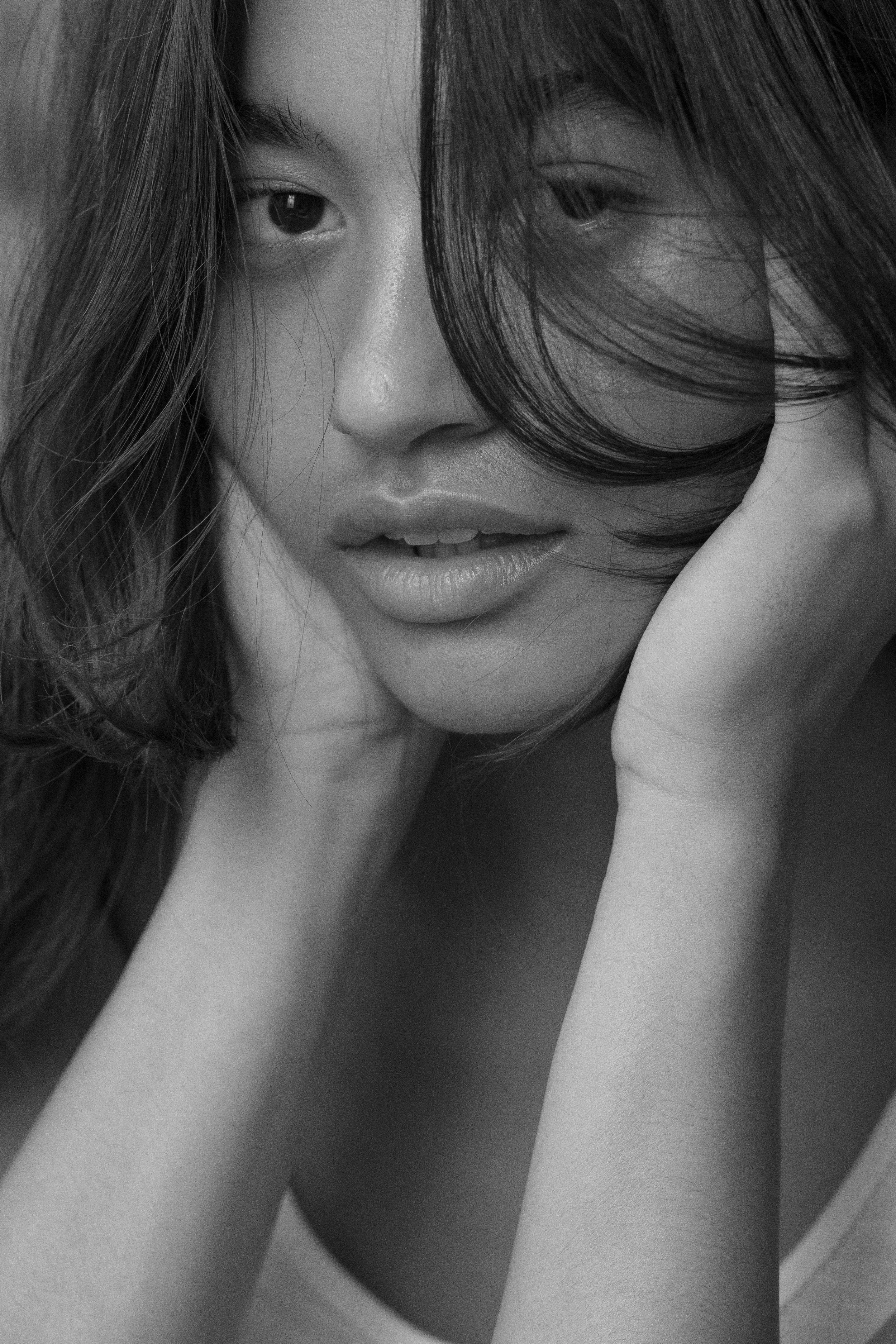 Close-up black and white portrait of a woman with long hair, resting her chin on her hand, with one eye partially covered by her hair.
