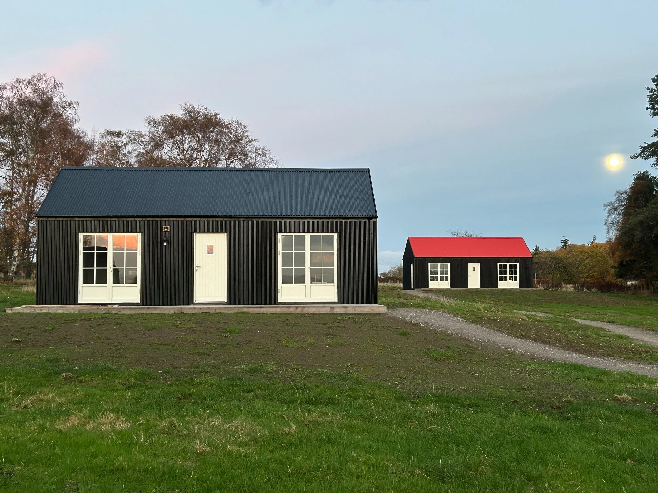 black cabins red roof at dusk autumn moon newly seeded wildflower meadow Scottish Highlands