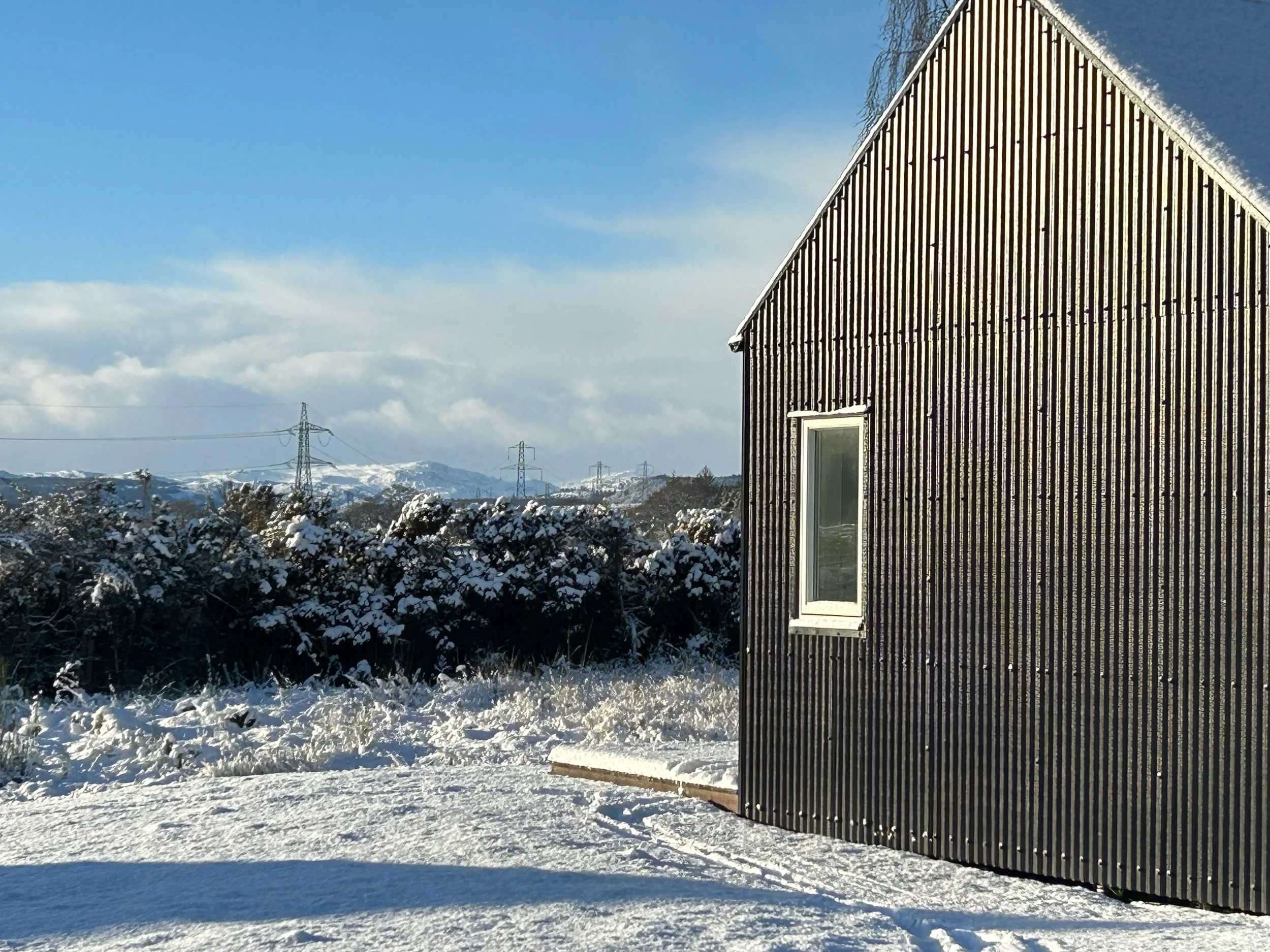 black tin cabin gable end looking towards mountains in snow Scottish Highlands