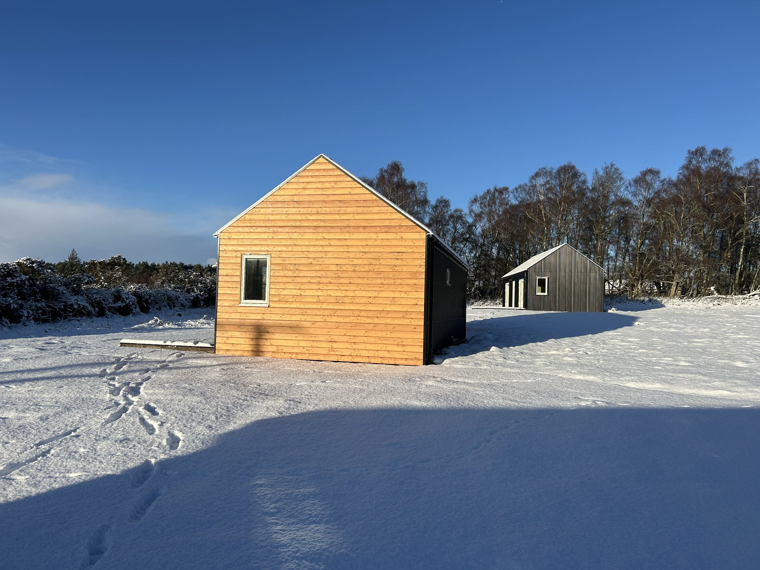 wooden gable of black tin cabin in snow and winter sunshine in Scottish Highlands