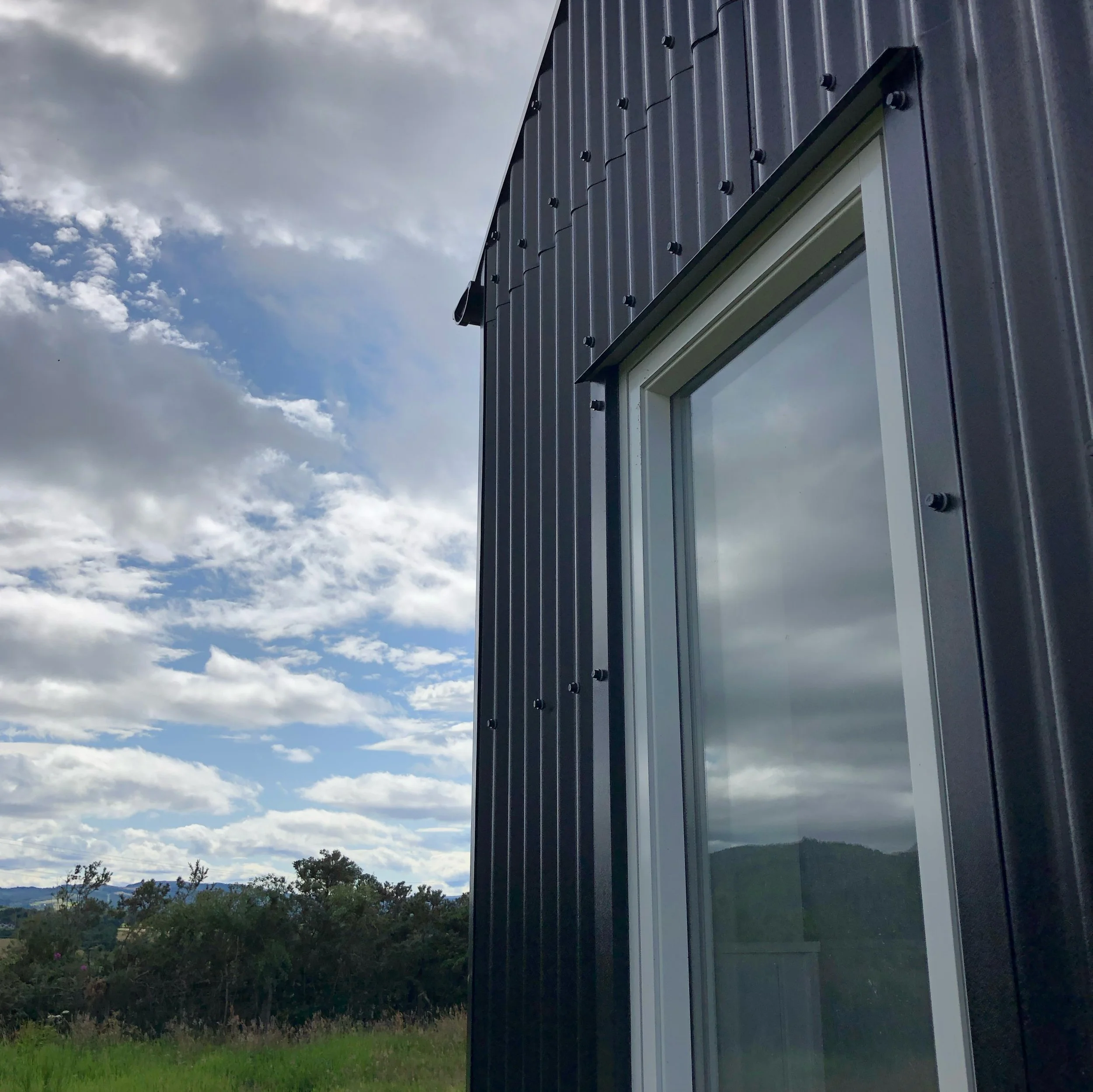 picture window of black tin cabin in meadow Scottish Highlands