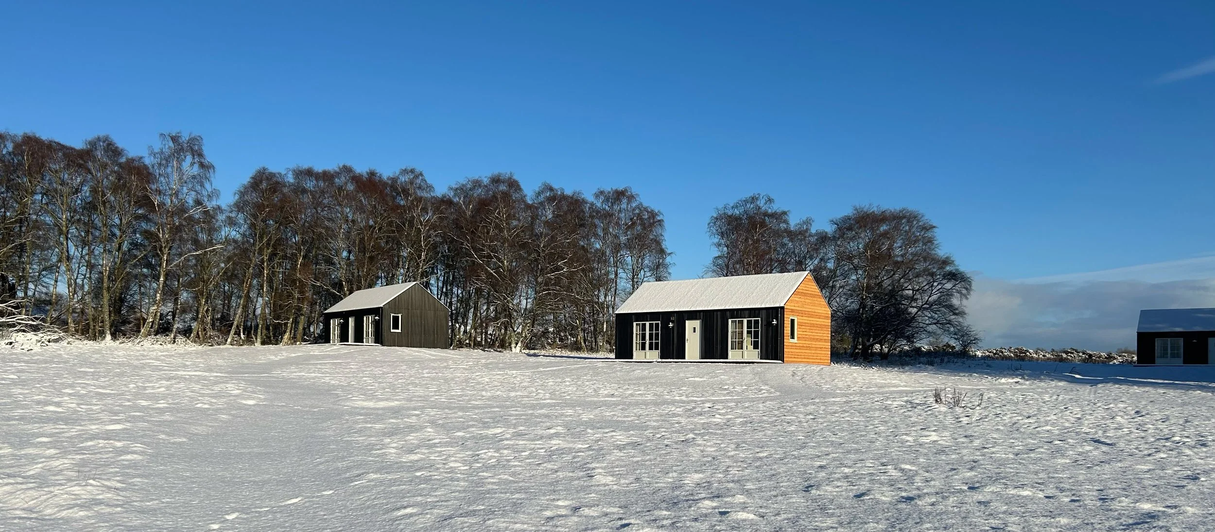 black tin and wood cabins in snow and winter sunshine in Scottish Highlands