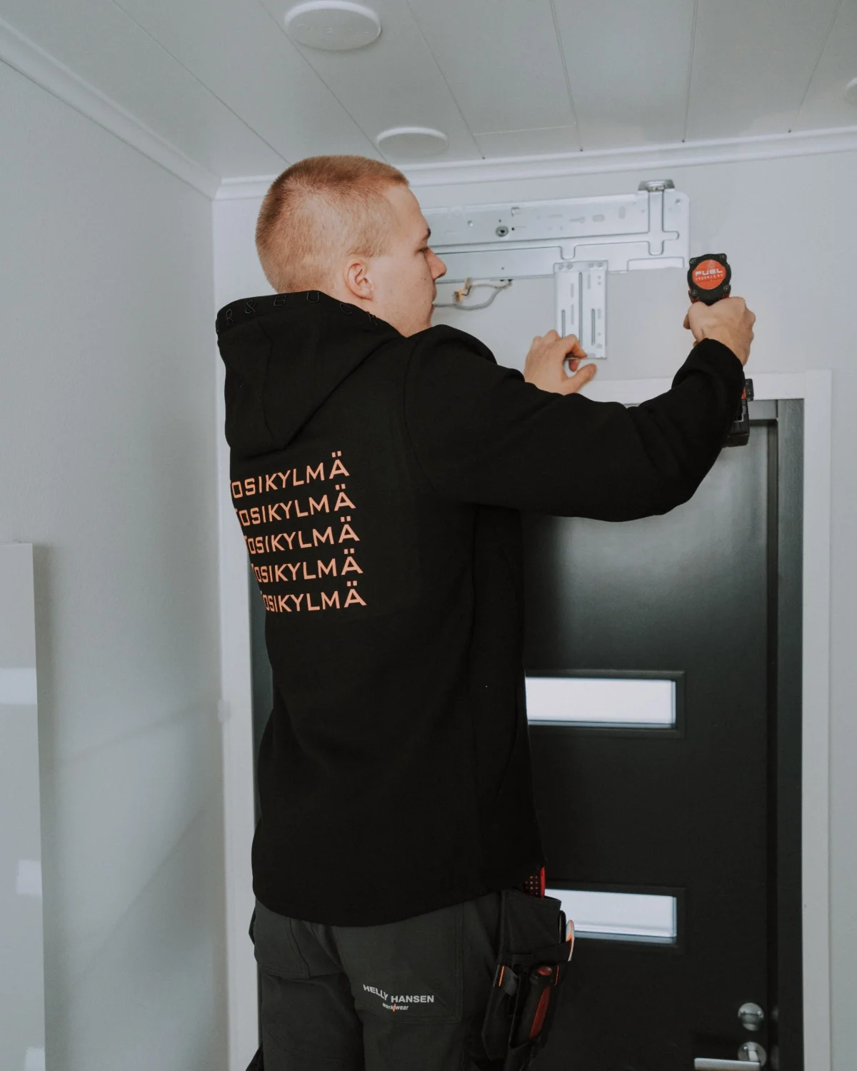 Mies asentaa sähkökaapin ovia, käyttäen ruuvimeisseliä seinälle.