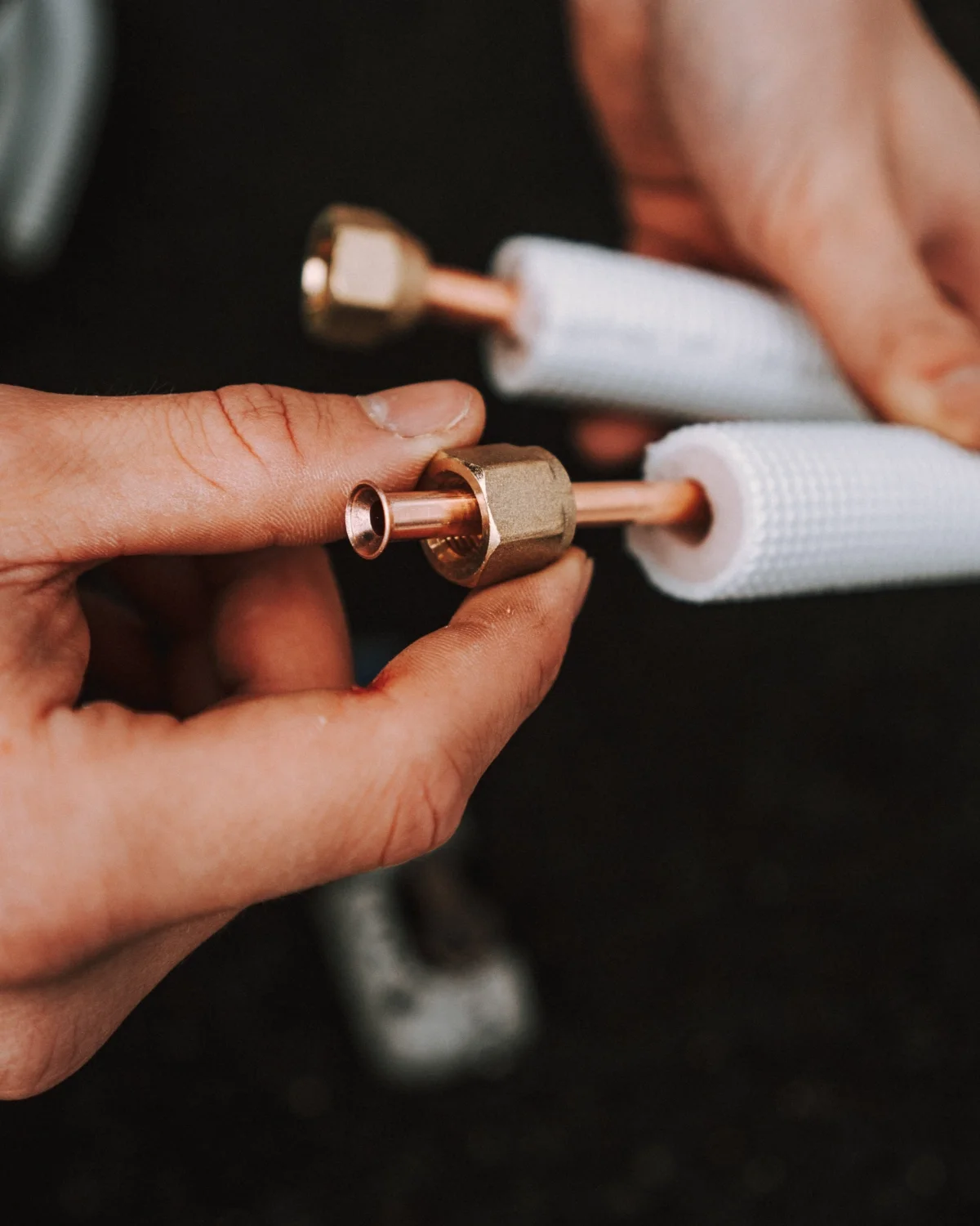 Kuvassa kädet käsittelevät kuparisia putkenosia ja metallisia liittimiä.