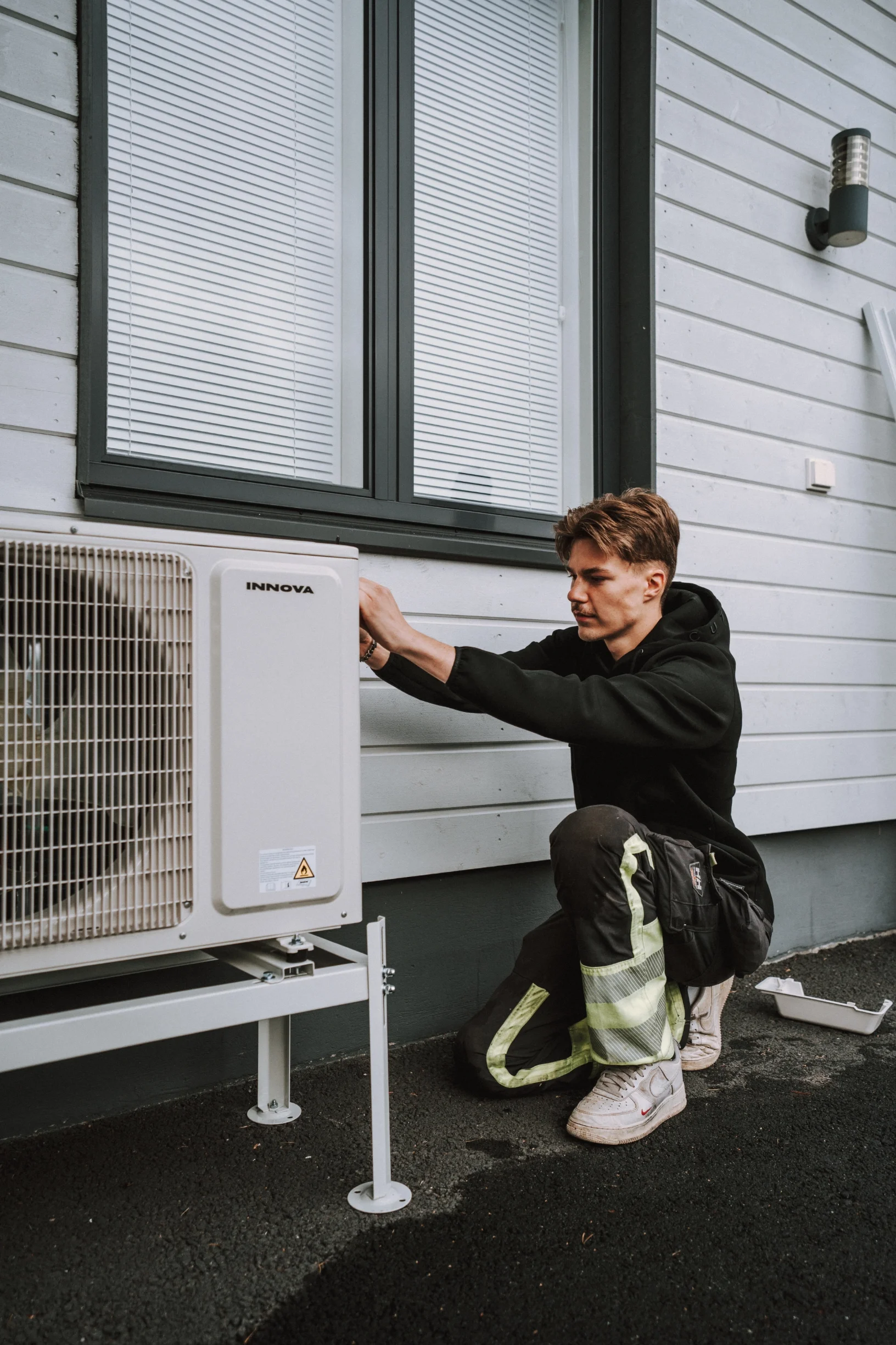 Nuori mies korjaa ulkoyksikköä talon seinustalla.