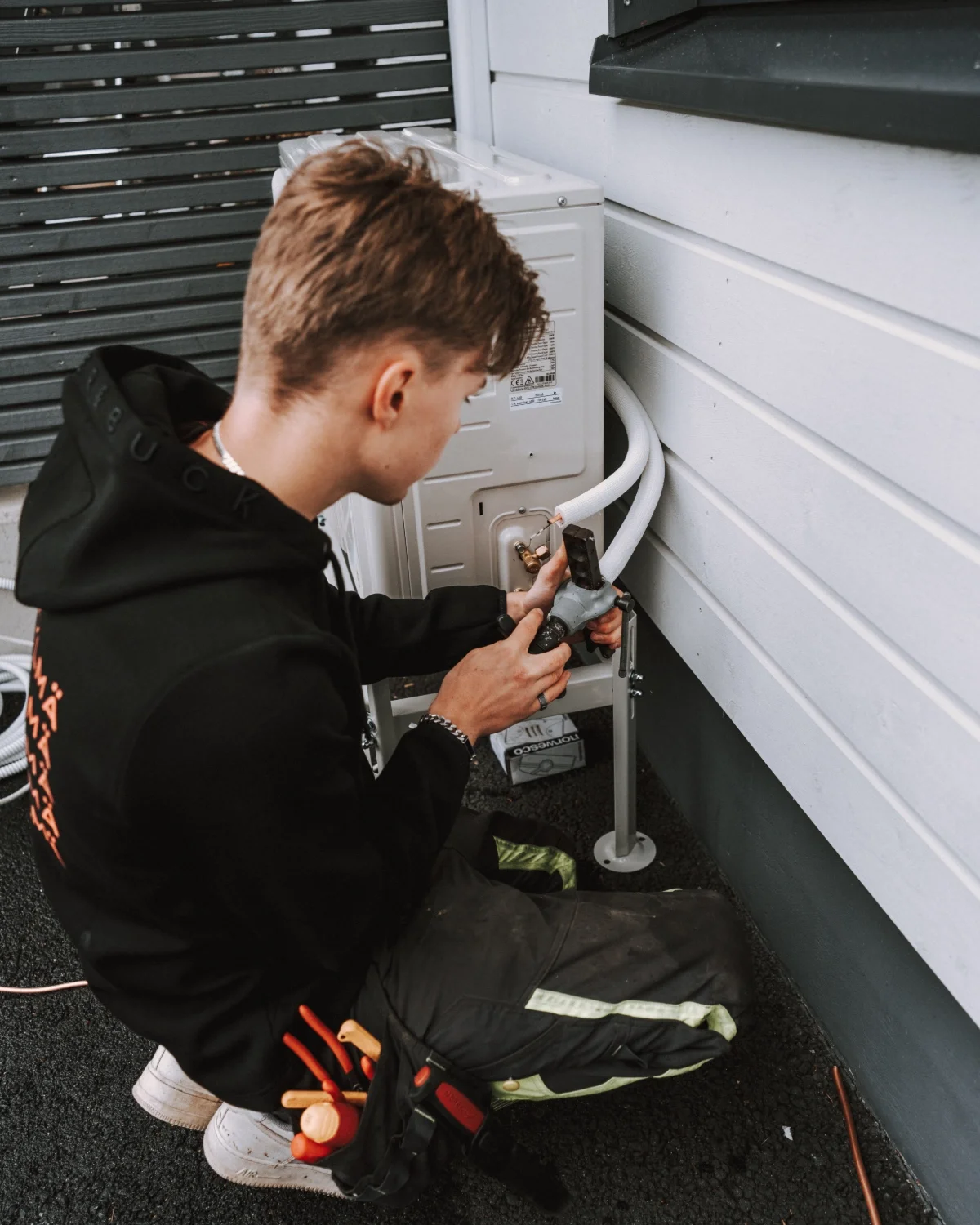 Nuori mies työskentelee ilmastointilaitteiston parissa ulkona.