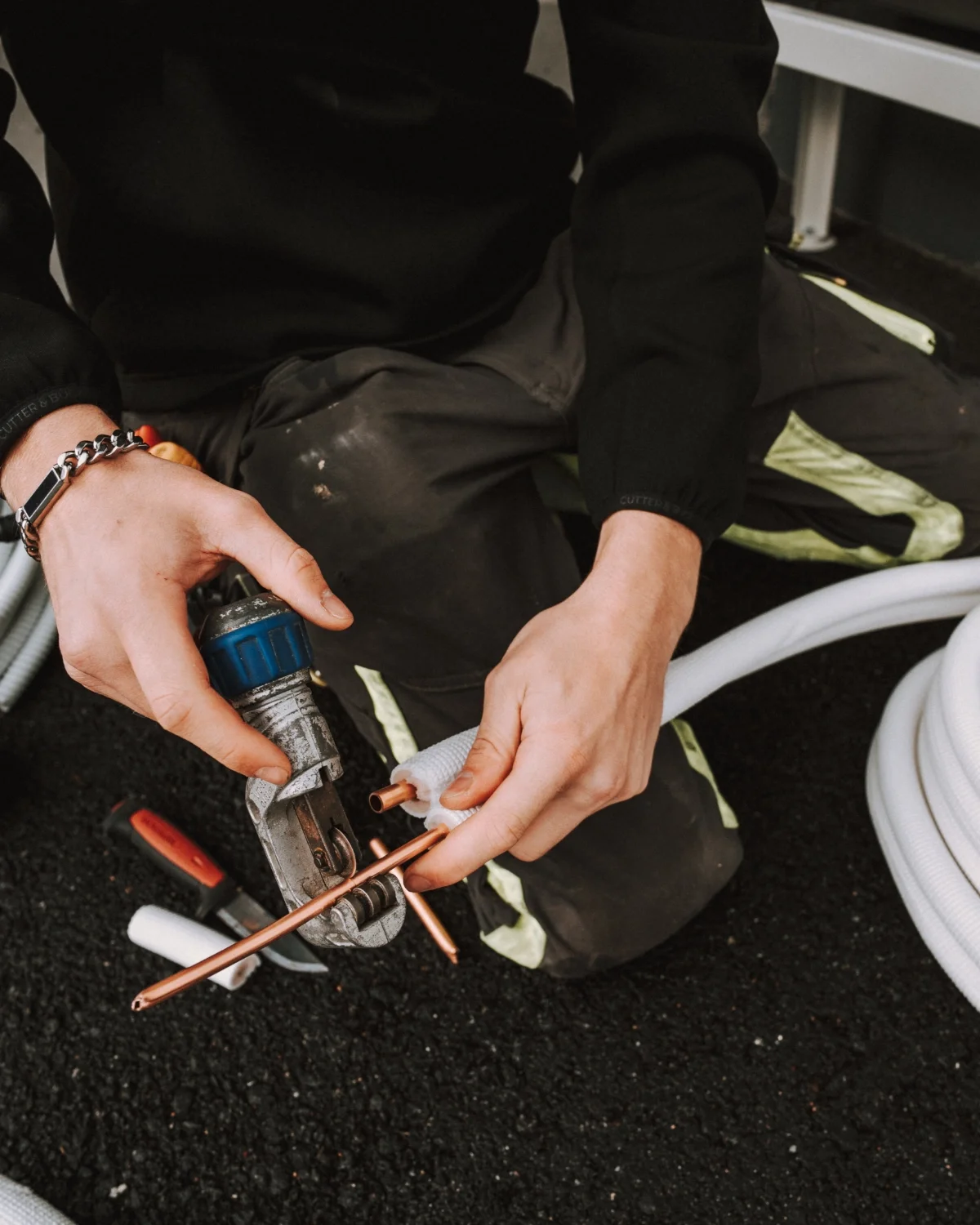 Henkilö tekee putkiremonttia käyttäen putkileikkuria ja kupariputkea.