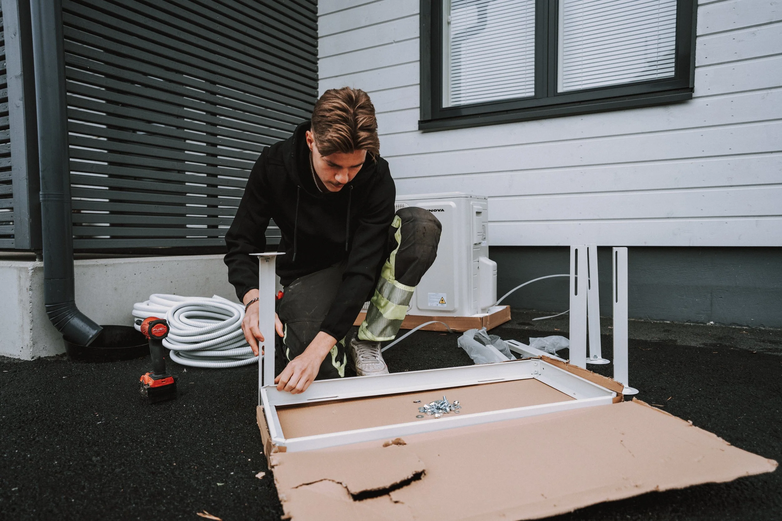 Nuori mies kokoaa huonekalua ulkona, ympärillä työkalut ja osat.