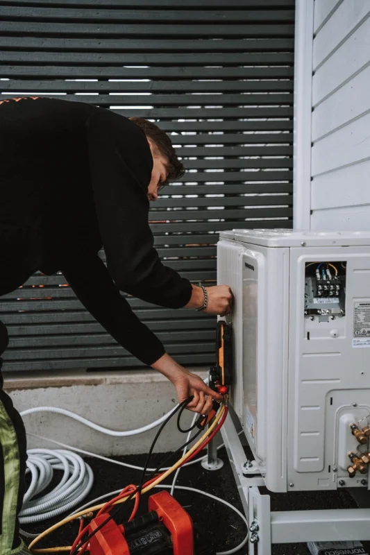 Henkilö asennassa ilmalämpöpumppua ulkona, taustalla pitkät puiset lattiapaneelit.