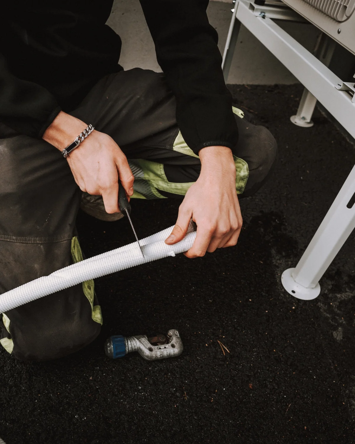 Henkilö työskentelee maaperän päällä käyttäen ruuvimeisseliä ja rukkasta, lähellä metallirunkoa ja mustaa maata.