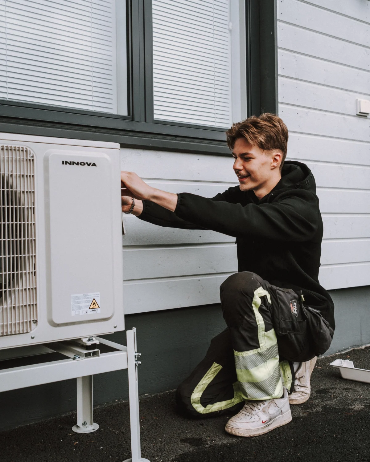 Nuori mies korjaa ilmalämpöpumppua ulkona talon seinää vasten.