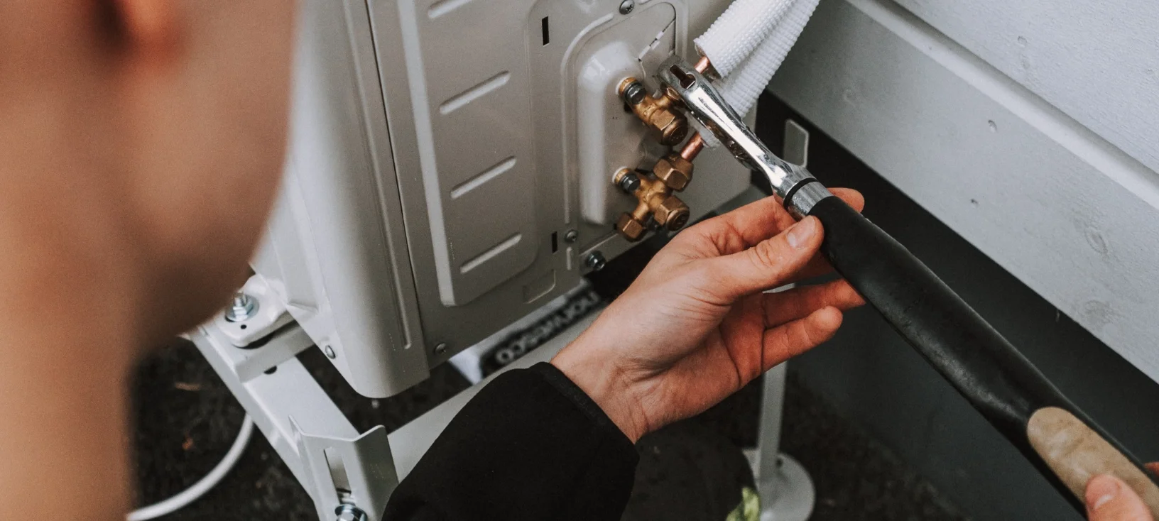 Henkilö korjaa ilmastointilaitteen yhteyksiä käyttäen talttapäistä jakoavainta.