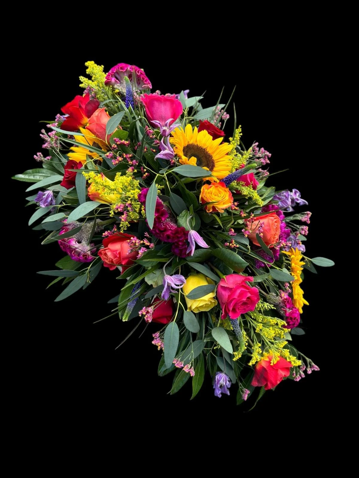 A colorful bouquet of various flowers including sunflowers, roses, lilies, and other blooms, arranged with green foliage against a black background.