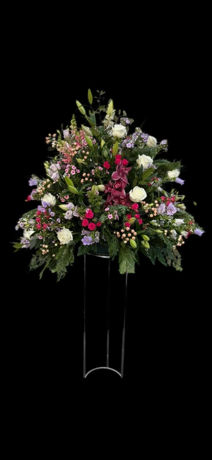 A floral arrangement with pink lilies, white roses, pink and lavender small flowers, and green foliage on a black background.