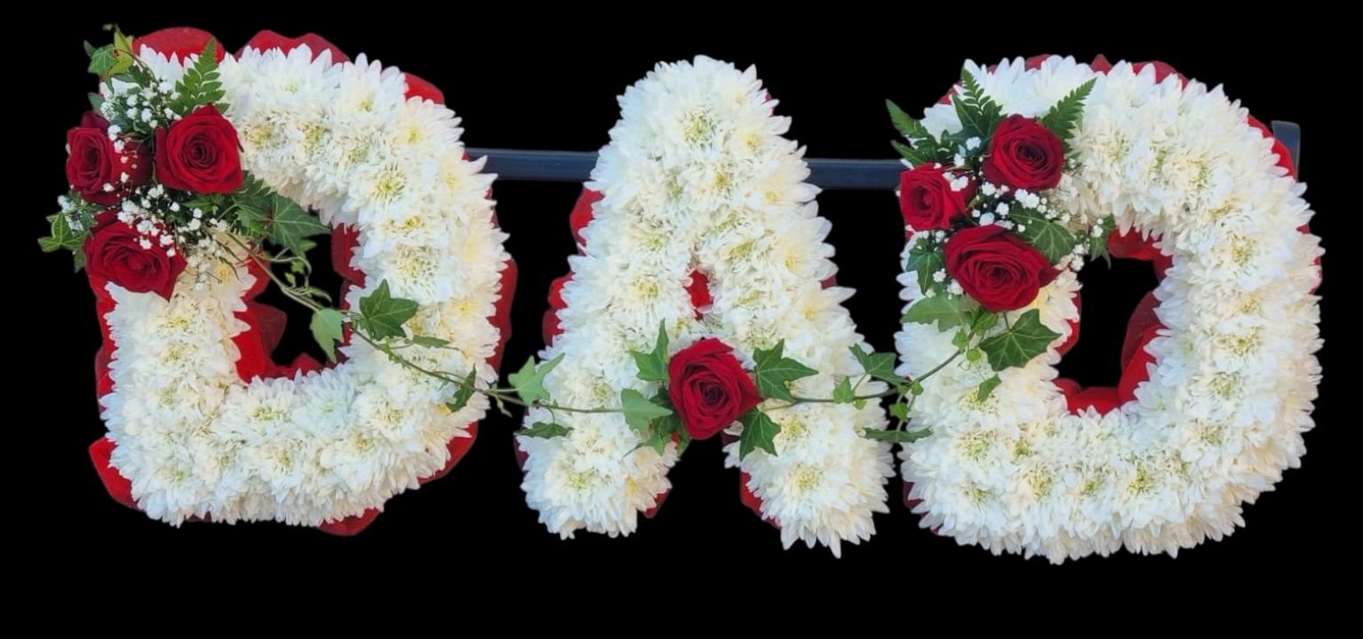 Floral arrangement spelling out the word 'DAD' with white flowers, red roses, and green leaves, set against a black background.