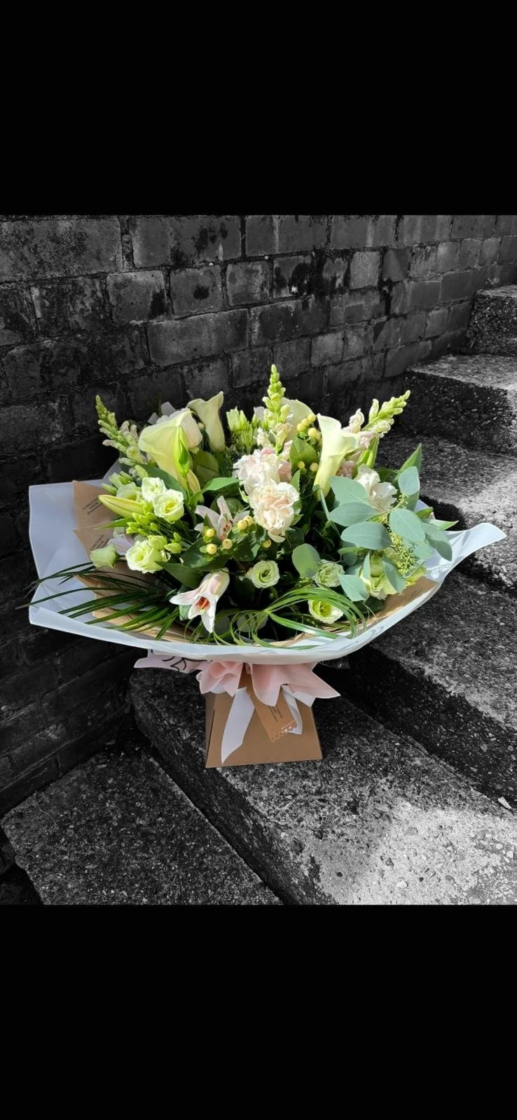 Bouquet of white and light pink flowers with greenery on stone steps and brick wall.