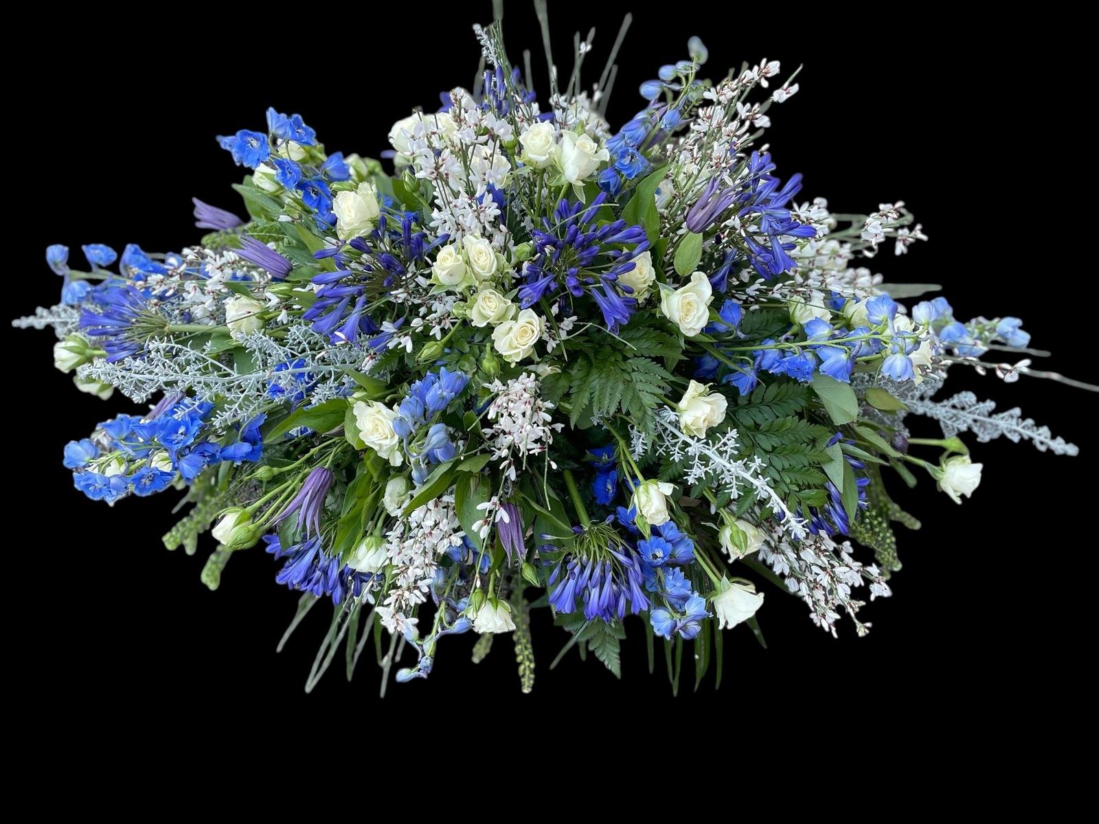 A bouquet of white roses, blue delphiniums, and other white and purple flowers with green leaves on a black background.