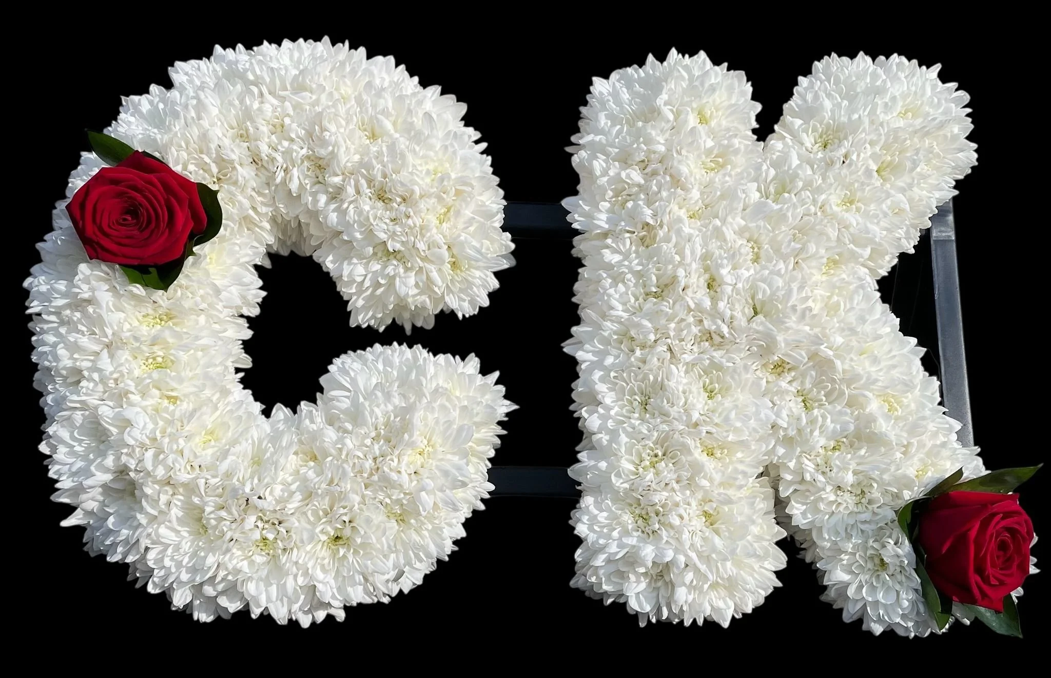 An arrangement of white chrysanthemums with a few red roses against a black background.