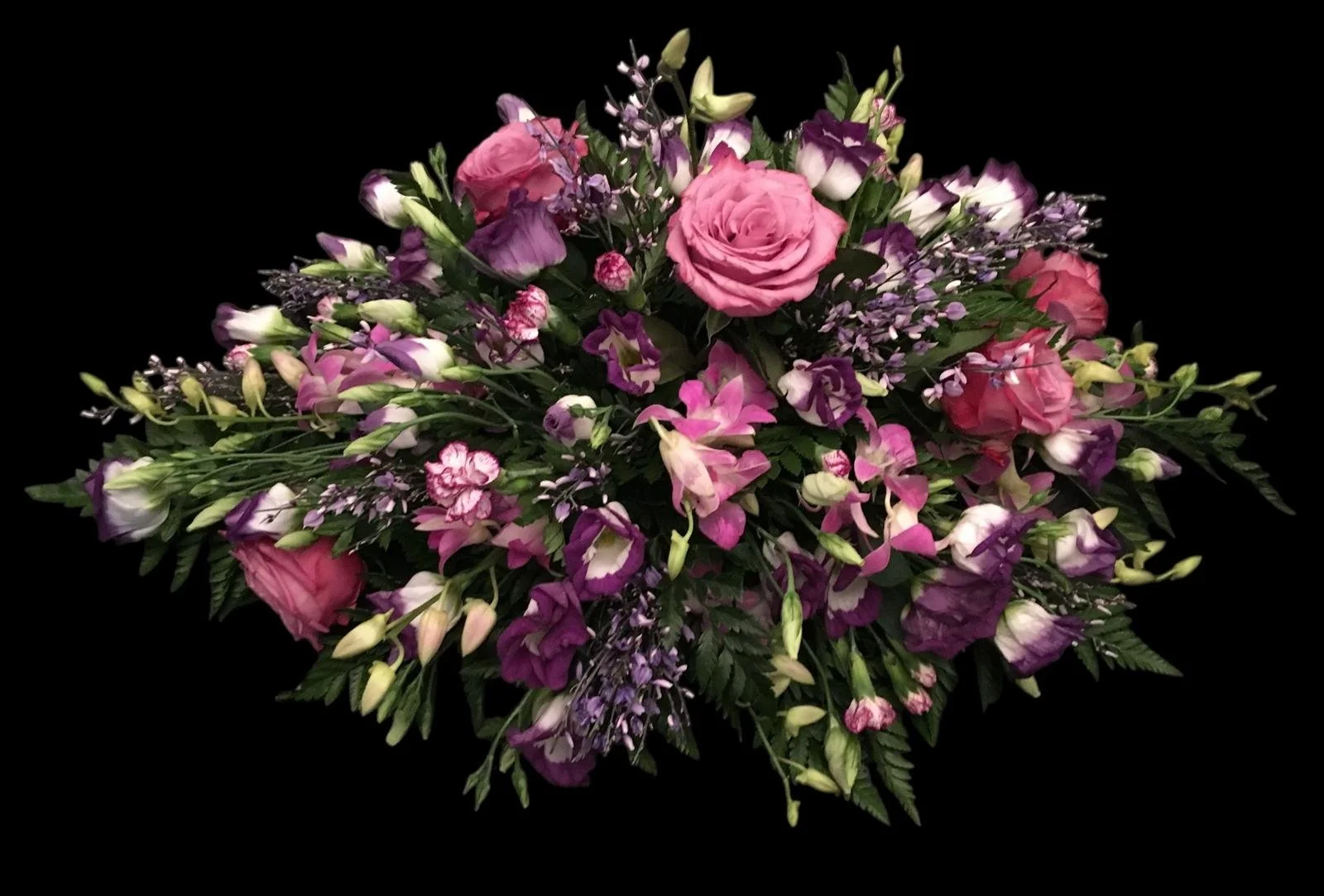 A large arrangement of pink and purple flowers, including roses and smaller blossoms, with green foliage, set against a black background.