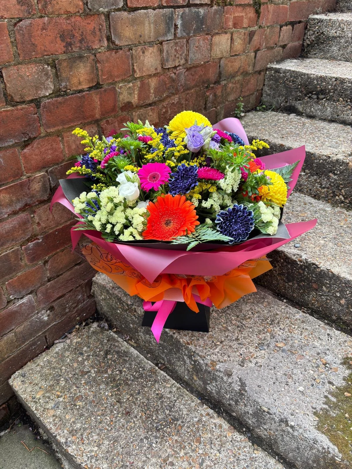 A colorful flower bouquet resting on outdoor concrete steps, with a brick wall in the background.