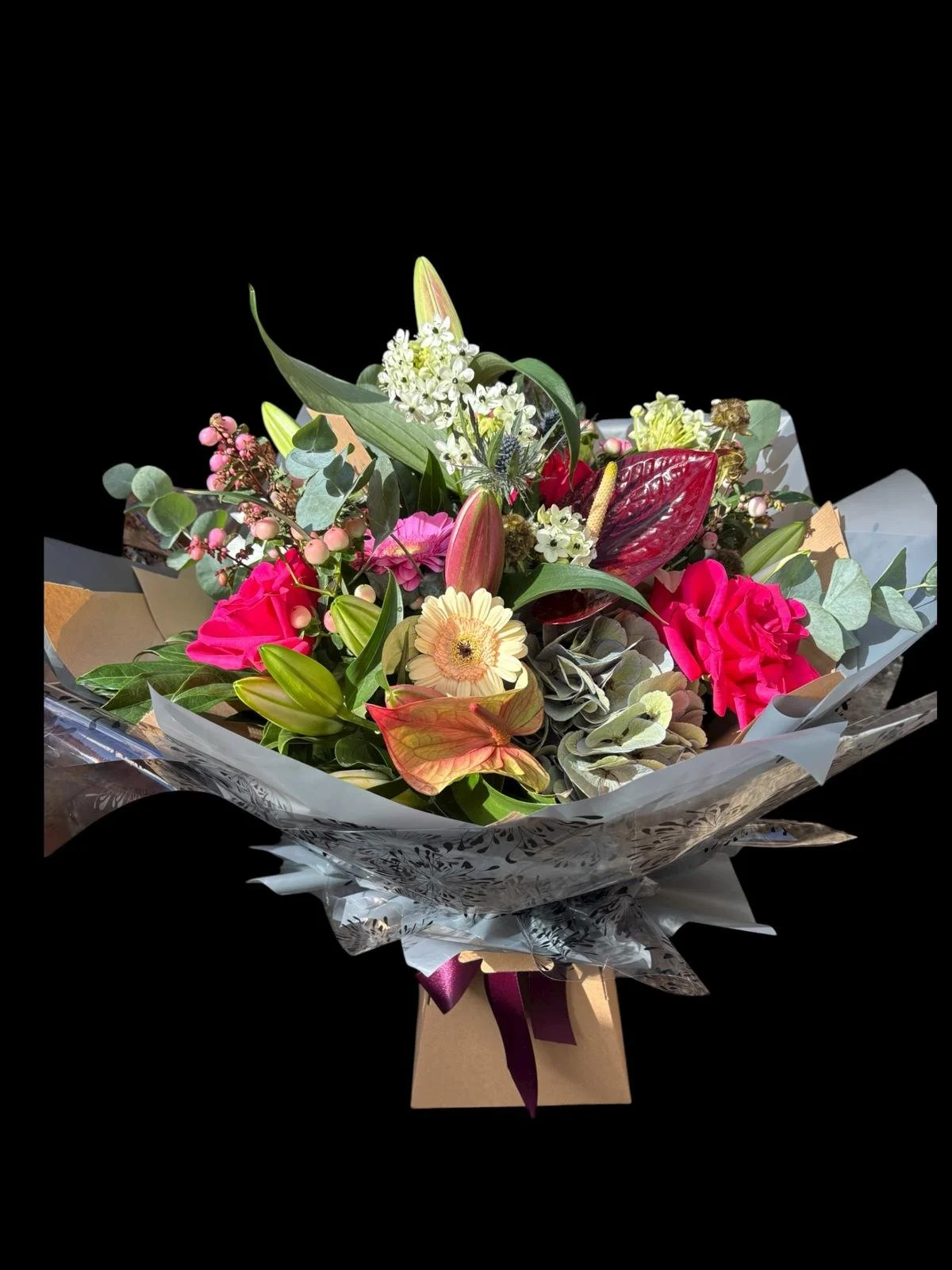 Colorful flower bouquet with pink, white, red, and cream flowers, wrapped in decorative paper with a ribbon.
