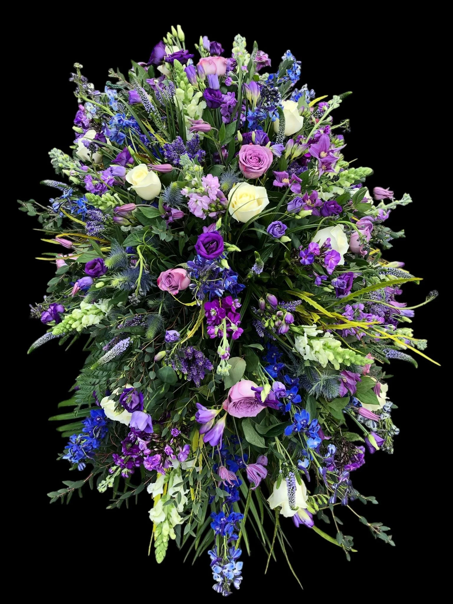 A large bouquet of purple, pink, white, and blue flowers with green foliage against a black background.