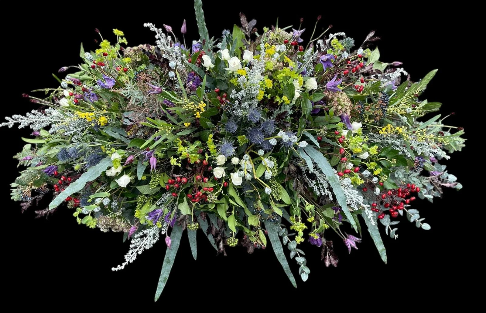A colorful floral arrangement with various flowers, green leaves, red berries, and purple accents on a black background.