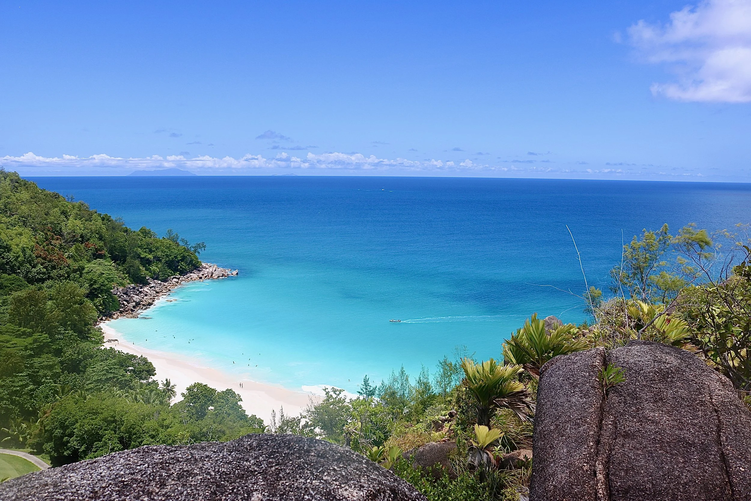 Blaue Bucht mit weißem Sandstrand, umgeben von grünen Hügeln und südlichem Ozean unter blauem Himmel