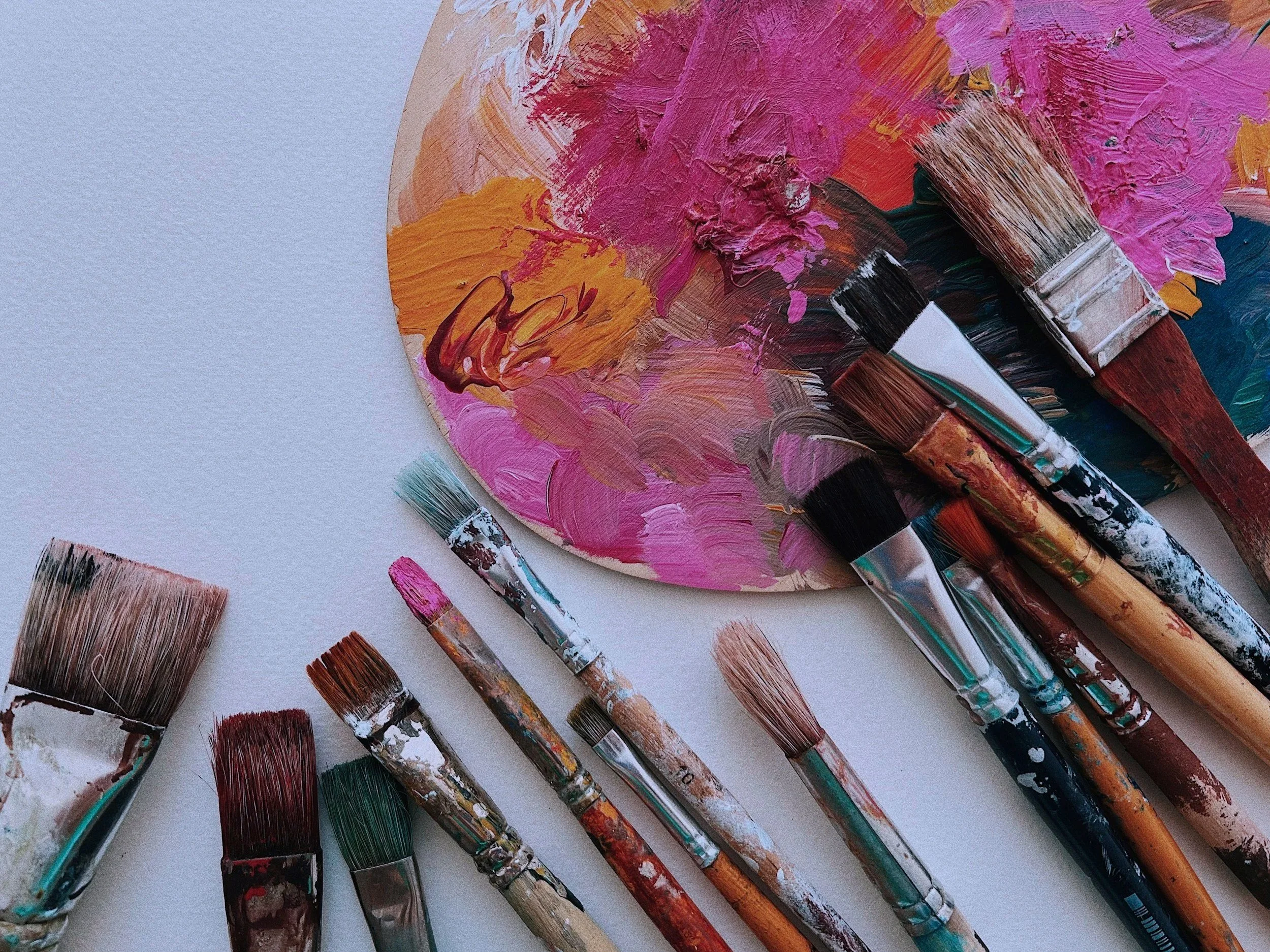 Paint palette with colorful dried acrylic paint and multiple used paintbrushes on a white surface.