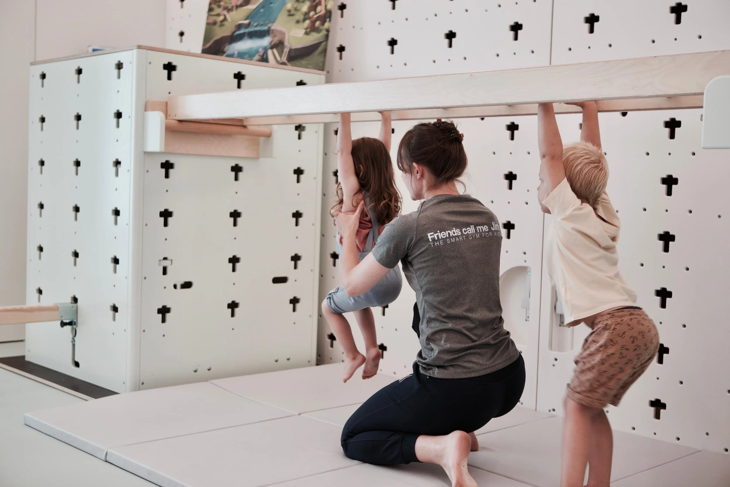 Een vrouw ondersteunt twee kinderen terwijl ze hangen aan een klimrek in een speellokaal.