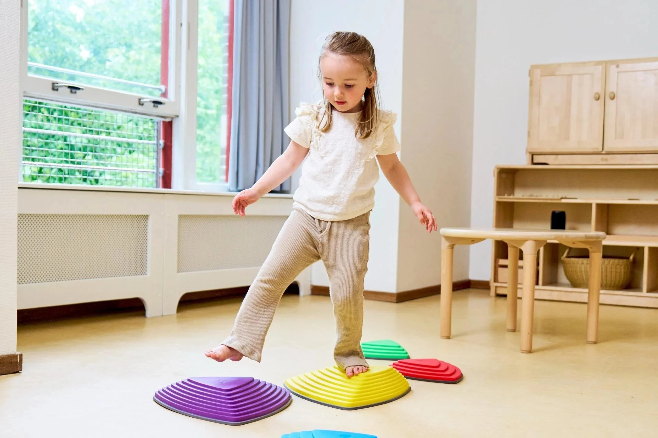 Een jong meisje die op gekleurde, schuine balansplaten in een speelkamer balanceert.