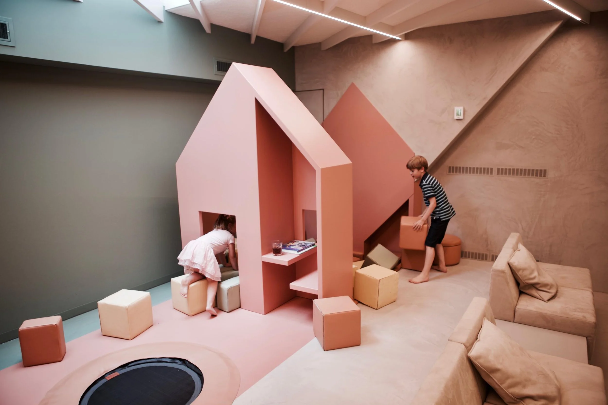 Twee kinderen spelen in een moderne woonkamer met pastelgekleurde meubels en een speelhuisje.