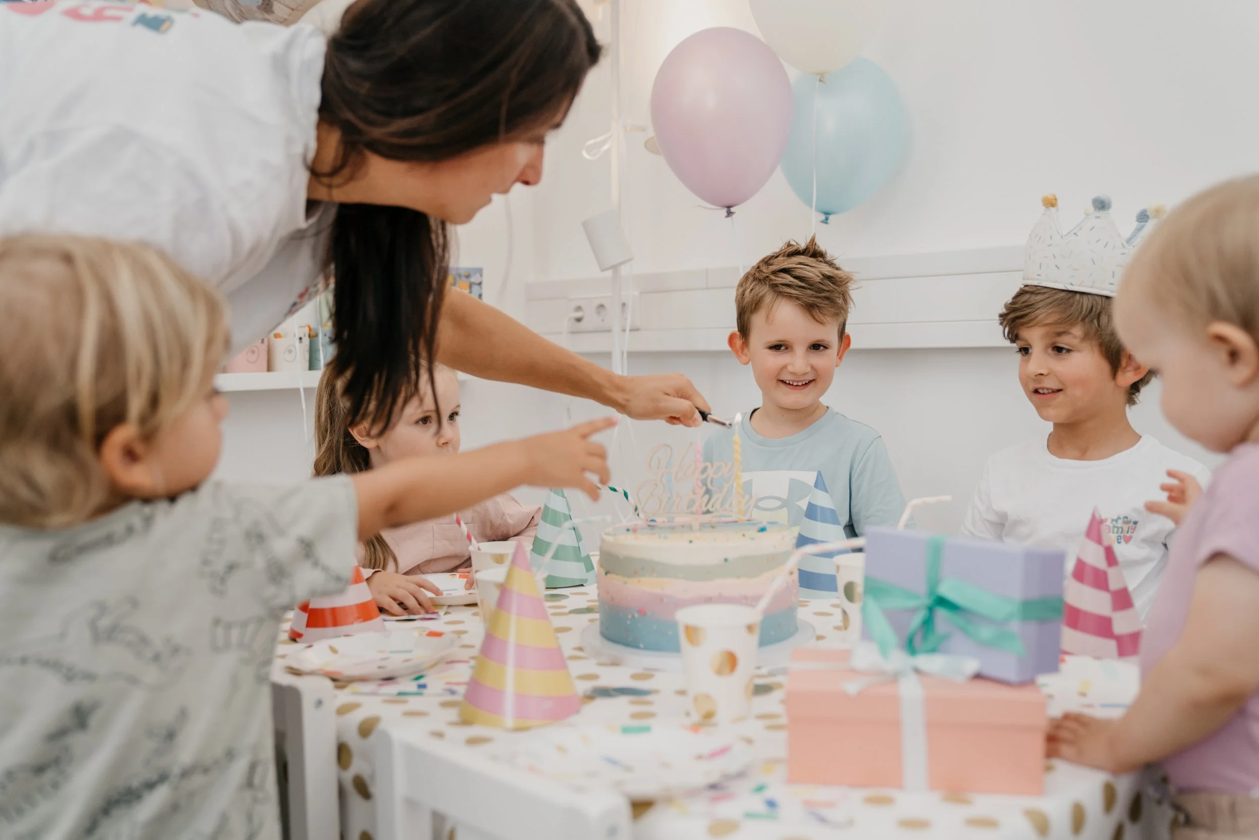 Kinder feiern Geburtstag mit einem Kuchen, Partyhüten und Ballons.