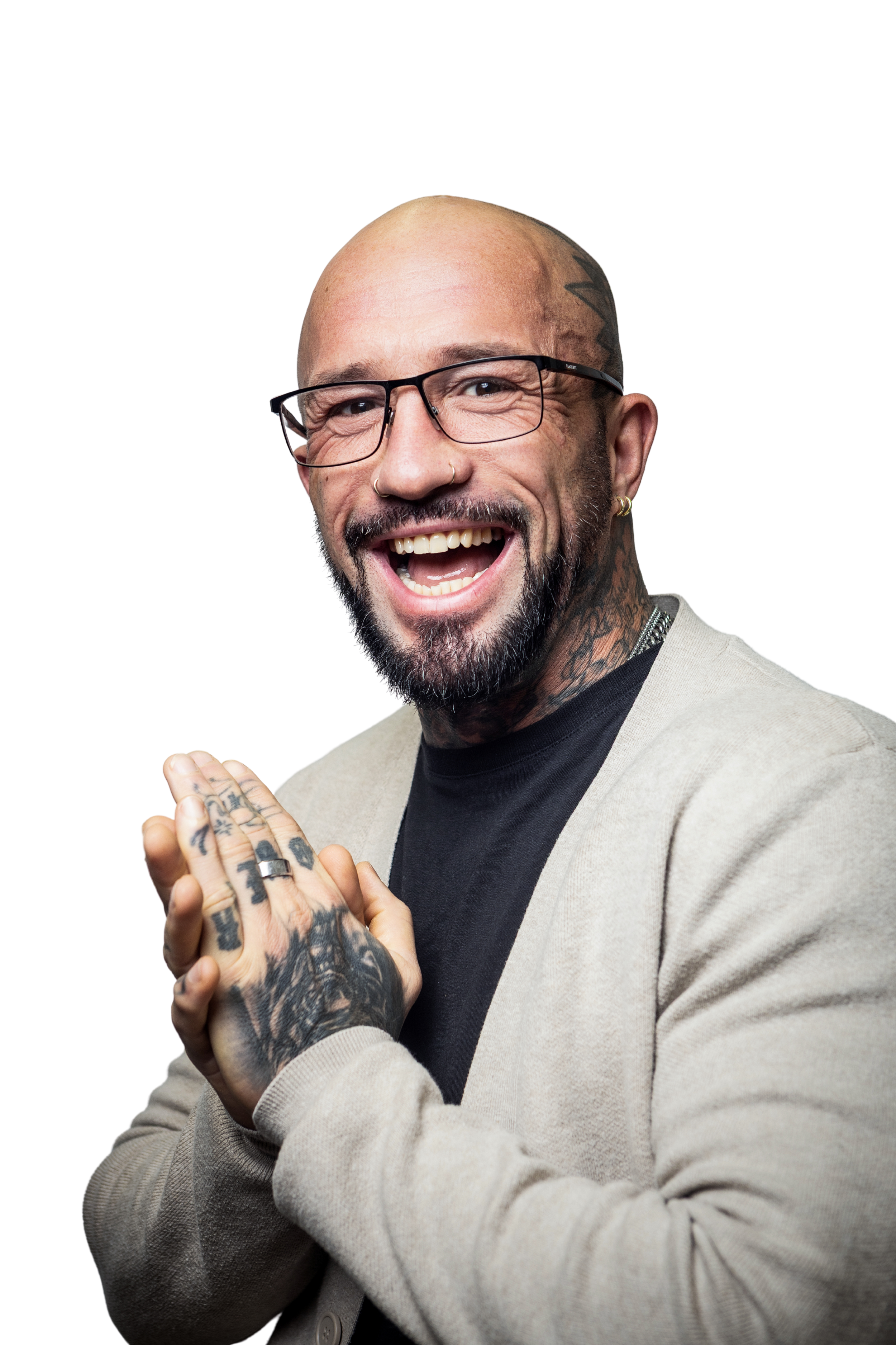 A smiling man with glasses, tattoos, and a beard, wearing a beige cardigan over a black shirt, claps his hands.