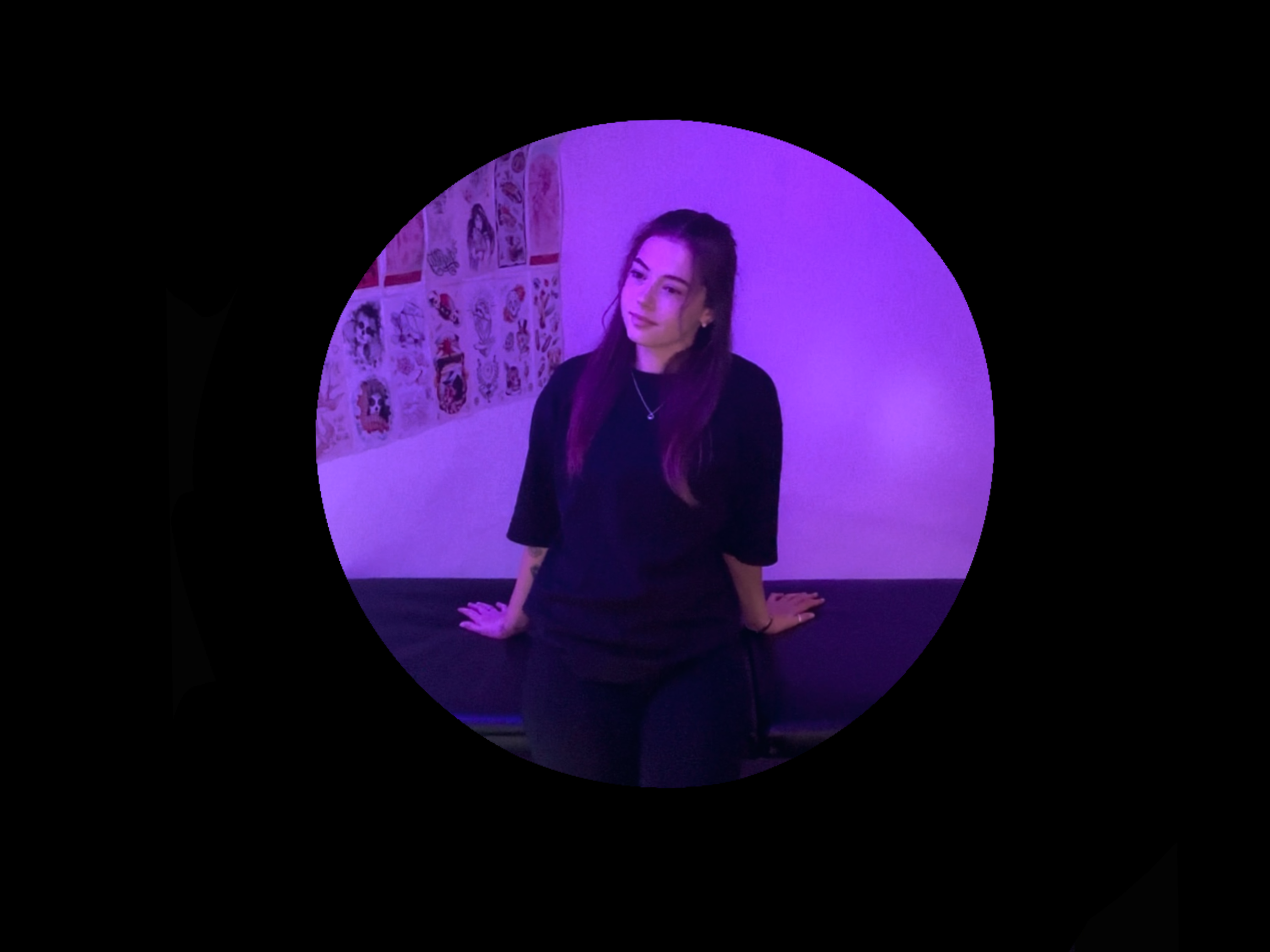 Young woman with long dark hair, sitting on a bench in a room with purple lighting, next to a wall decorated with cartoon posters.