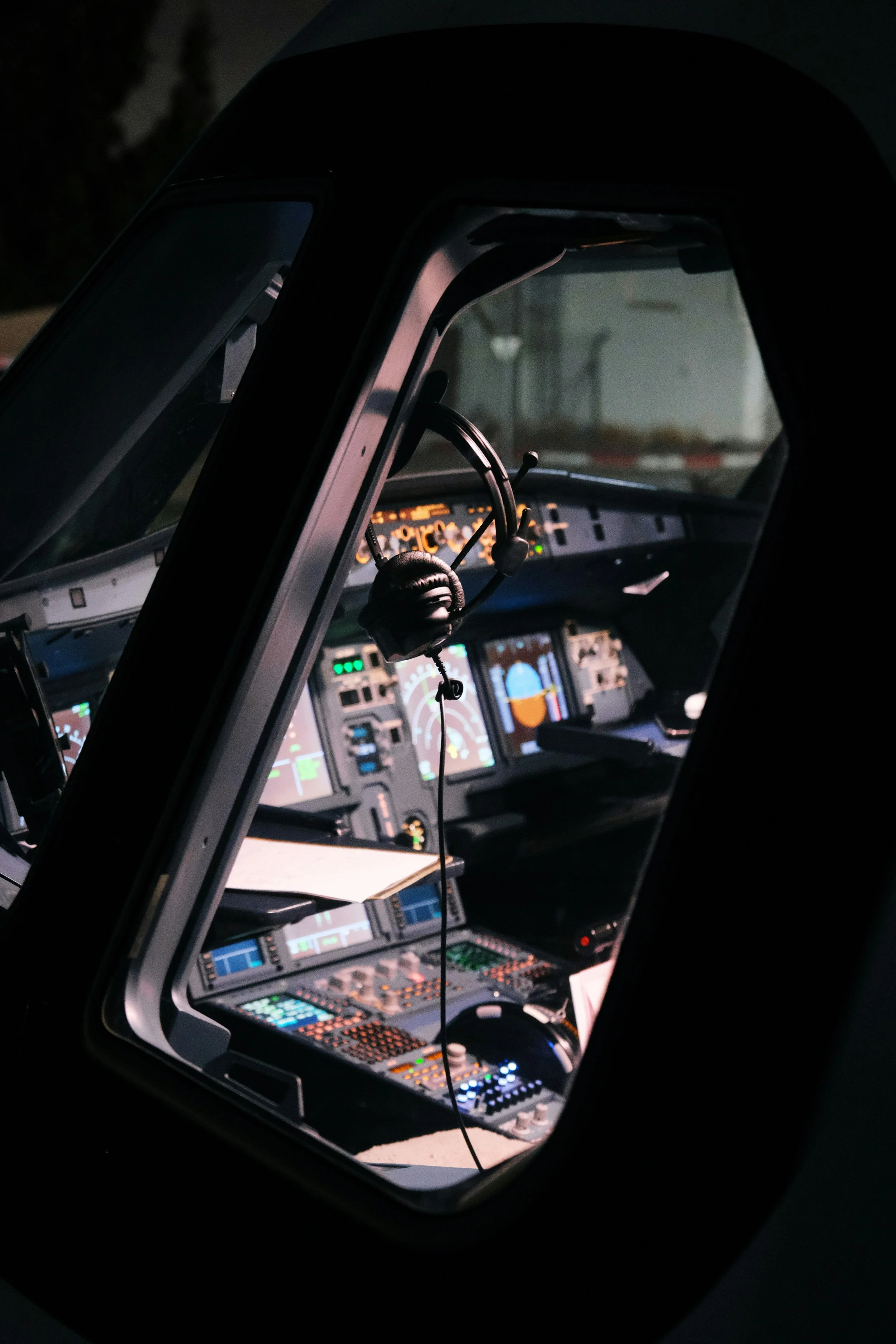Inside view of an airplane cockpit showing various instruments, screens, and controls with a headset hanging from the control panel.