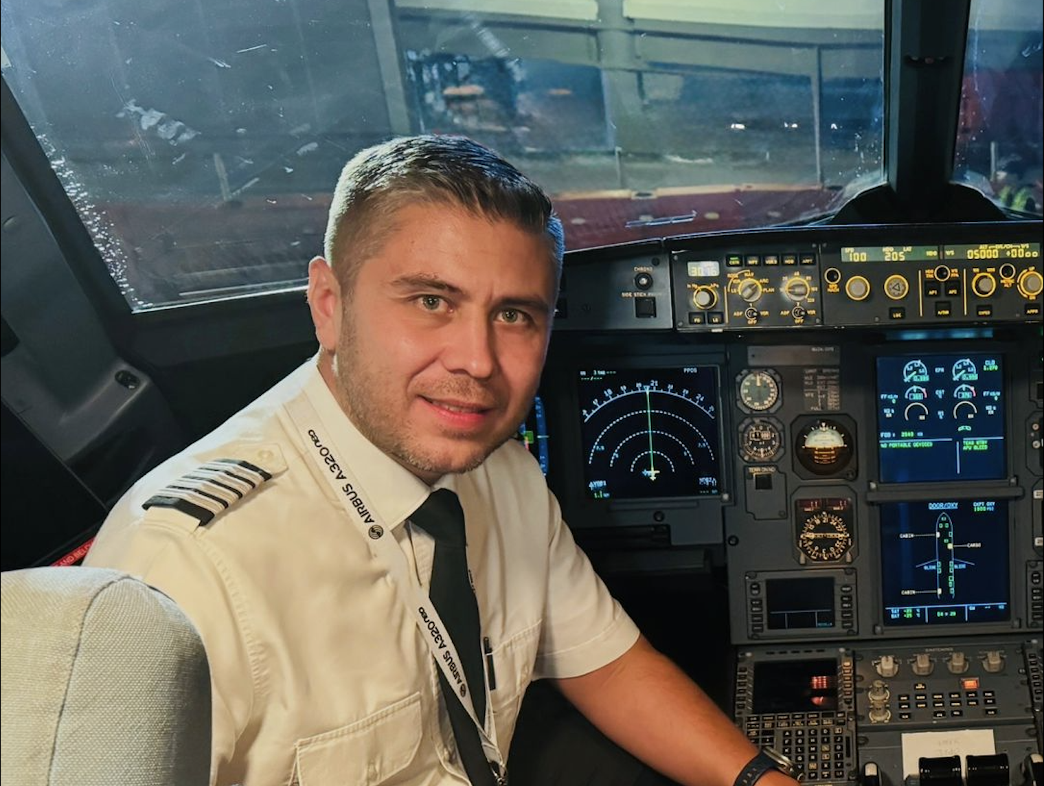A male pilot in uniform sitting in the cockpit of an airplane with various instruments and displays around him.