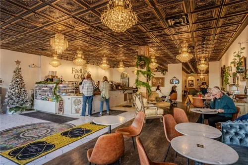 Interior of a cozy cafe with ornate ceiling, chandeliers, decorated Christmas tree, and customers seated at tables, some ordering at the counter.